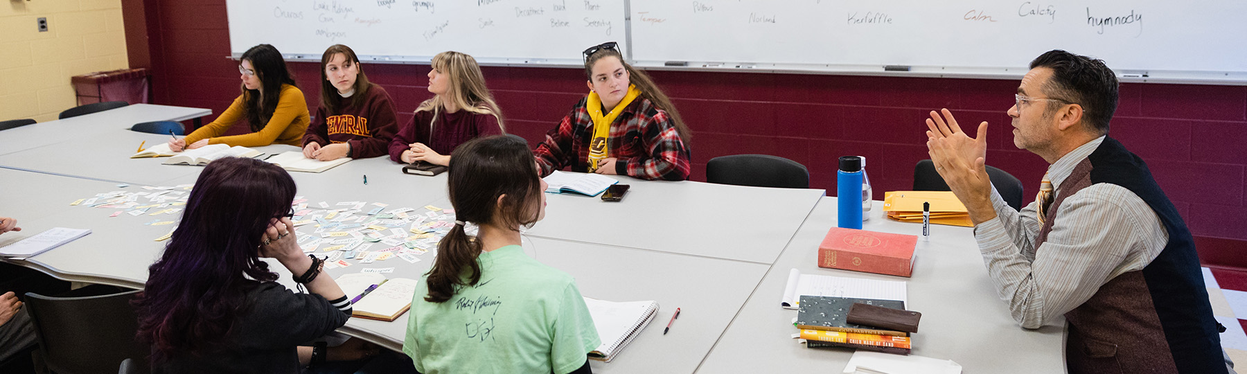 English faculty member Robert Fanning and six students sit at table with stacks of books and papers.