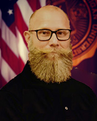 Closeup image of Bryan P. Boykin wearing dark coat in front of American flag and Central Michigan University flag.