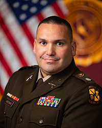 Closeup image of LTC Ryan Greening wearing a military uniform with a U.S. flag and CMU flag in the background.