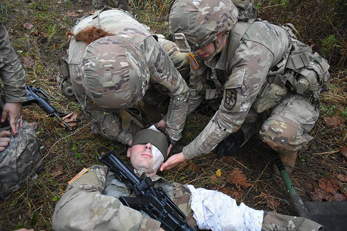 Cadets wearing Army uniforms place a bandage on another cadet's head