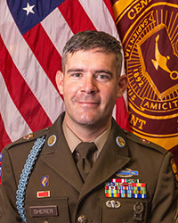20250513_SFC_Neill_Sherer_200x250 Closeup image of SFC Neill Sherer wearing his military uniform with the American and Central Michigan University flags behind him.