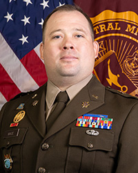 20250617_MAJ_Christopher_Mace_200x250 Closeup image of MAJ Christopher Mace wearing his military uniform with the American and Central Michigan University flags behind him.