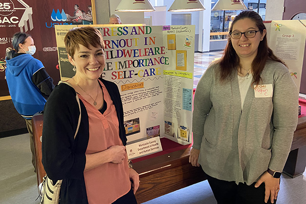 Social Work student stands next to her field placement supervisor and a poster display that describes her field placement experiences.