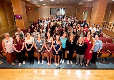 Students and faculty at the annual Social Work Convocation Ceremony all standing and looking up at the camera in the front of the auditorium.