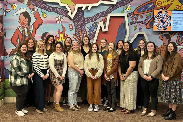 Central Michigan University Social Work students stand in two rows in front of a colorful Native American mural.