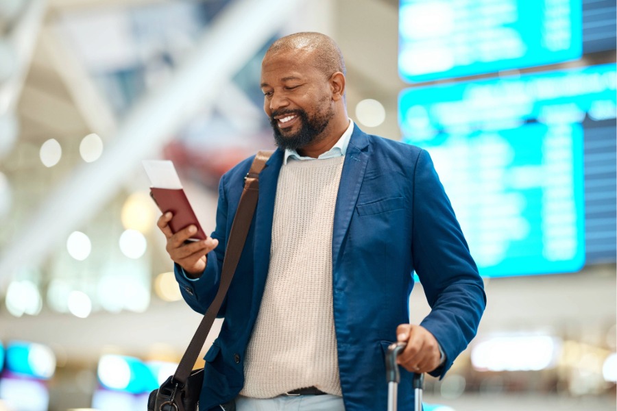 A man holding a passport and looking at his phone in an airport.