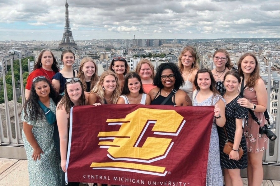 A group of students posing for a photo with a CMU flag in front of the Eiffel Tower