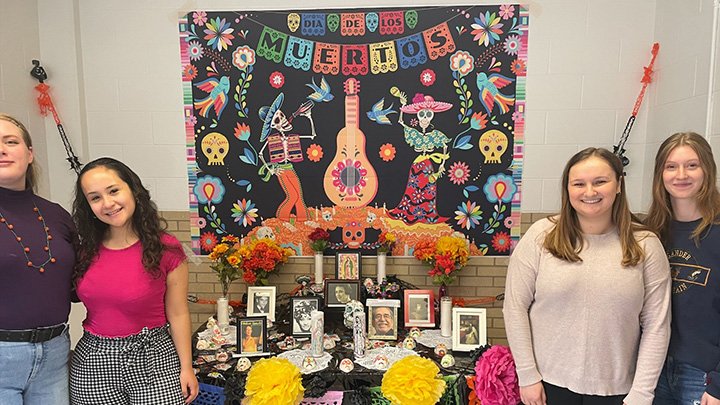 Students from the CMU Spanish Club stand next to ofrendas with framed pictures, candles and flowers for Día de los Muertos (Day of the Dead).