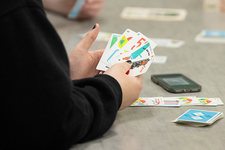 Close up image of an individual's arms wearing a black shirt and holding a cards from a game