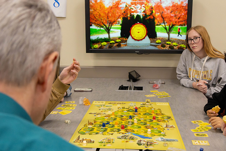 Image of a group of individuals seated around a yellow board game with yellow game cards and dice on the table in front of them.