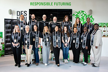 Alejandra Rengifo stands with other Faculty Innovation Fellows in two rows in front of a banner and a large television screen.