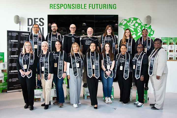 Alejandra Rengifo stands with other Faculty Innovation Fellows in two rows in front of a banner and a large television screen.