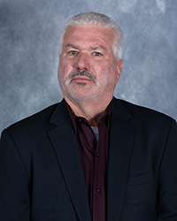 Don Uzarski wears a jacket, collared shirt and tie while posing for a headshot.