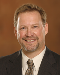 Tom Gehring wears a jacket, collared shirt and tie while posing for a headshot.