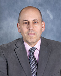 Stephen Juris wears a jacket, collared shirt and tie while posing for a headshot.
