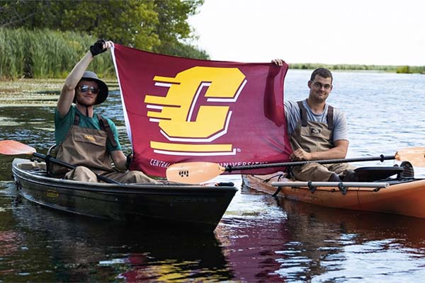 Two conservation students on kayaks holding a Central Michigan University flag.