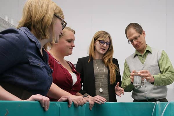 Three students and a biology faculty member standing around a tank while examining a sample in the aquatic vivarium