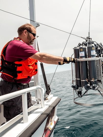 Researcher lowering equipment from the M V Chippewa into the water