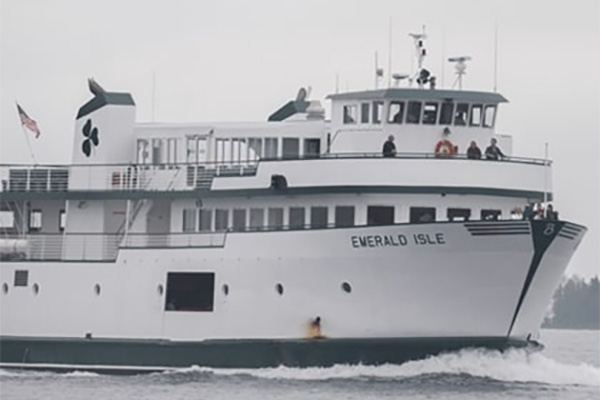 A large boat on the water. the boat has thee tiers of decks and several people standing at the front.