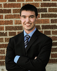 Eric Urbaniak in front of a brick wall, wearing blue suit, smiling at the camera.