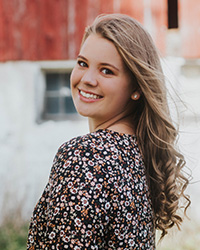 Meghan VanDamme in a floral dress smiling at the camera over her shoulder.