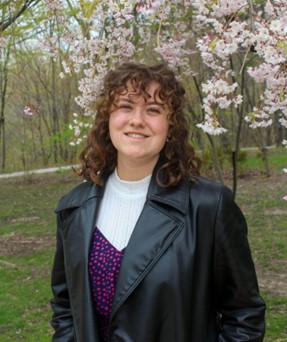 Ava Brewer in a black coat in front of a blossom tree
