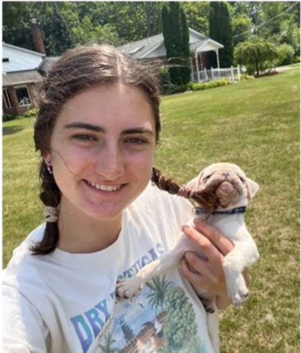 Claire DeBlanc holding a  puppy in a grassy field.