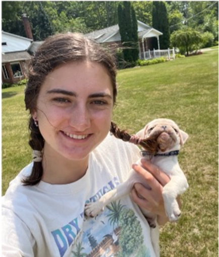 Claire DeBlanc holding a puppy in a grassy field.