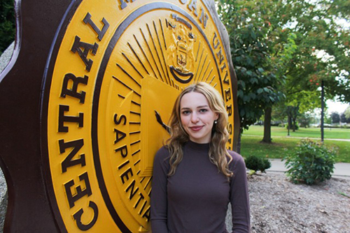 Tiffany Jurge in a dark sweater in front of the CMU Seal.
