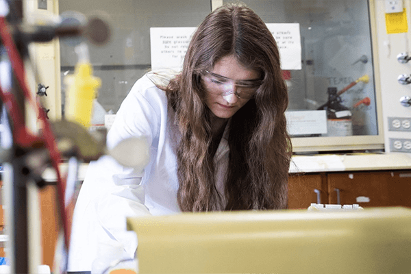Female student in a lab coat examines research materials.