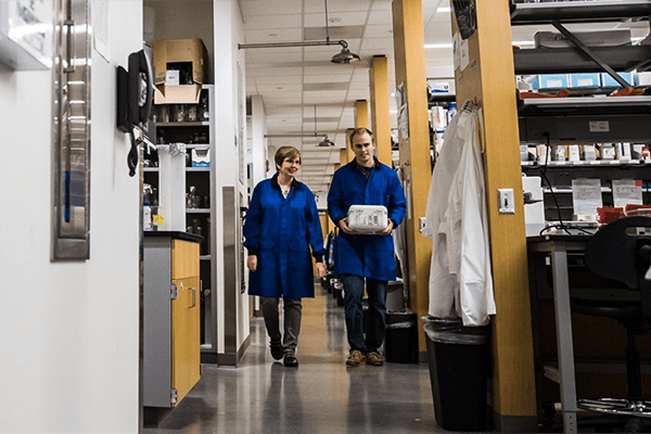 A female professor and male student walk down an aisle in the biochemistry lab.