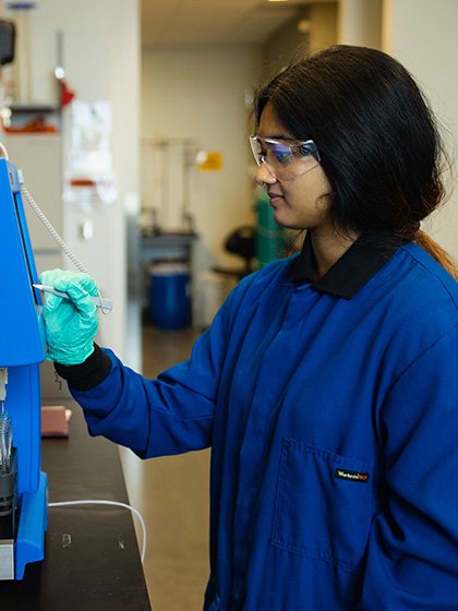 A student wearing safety goggles entering data into a machine.