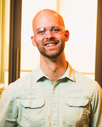 Ben Swarts in a khaki colored button up shirt, wearing safety goggles, smiling at the camera.