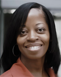 Angle Bush wears an orange blouse and smiles at the camera.