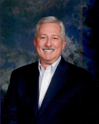 A man with white hair and a mustache wears a white shirt and sport coat.