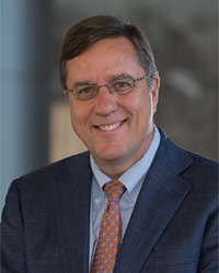 Robert Richard in a blue shirt, red tie, and blue suit smiling at the camera.