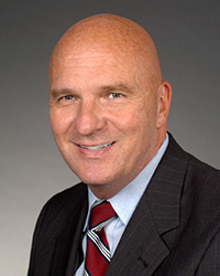 A man in a suit and tie against a neutral backdrop.