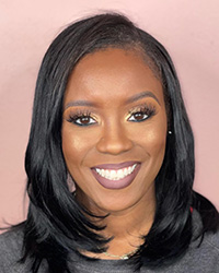 A woman with long black hair smiling in front of a neutral background.