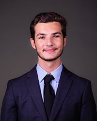 A man in a blue suit and tie in front of a dark backdrop.