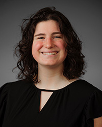 A woman with dark hair wearing a black shirt in front of a grey backdrop.