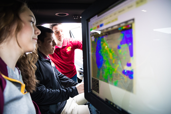 Students and faculty member examining weather map inside the CMU mobile weather station, MESONET.
