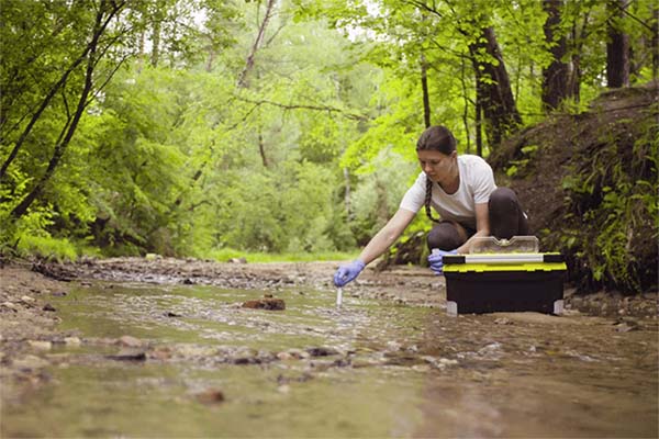 Environmental science student taking water samples in a river.