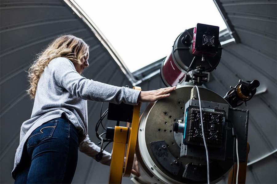 A student stands next to a telescope in the Brooks Astronomical Observatory.