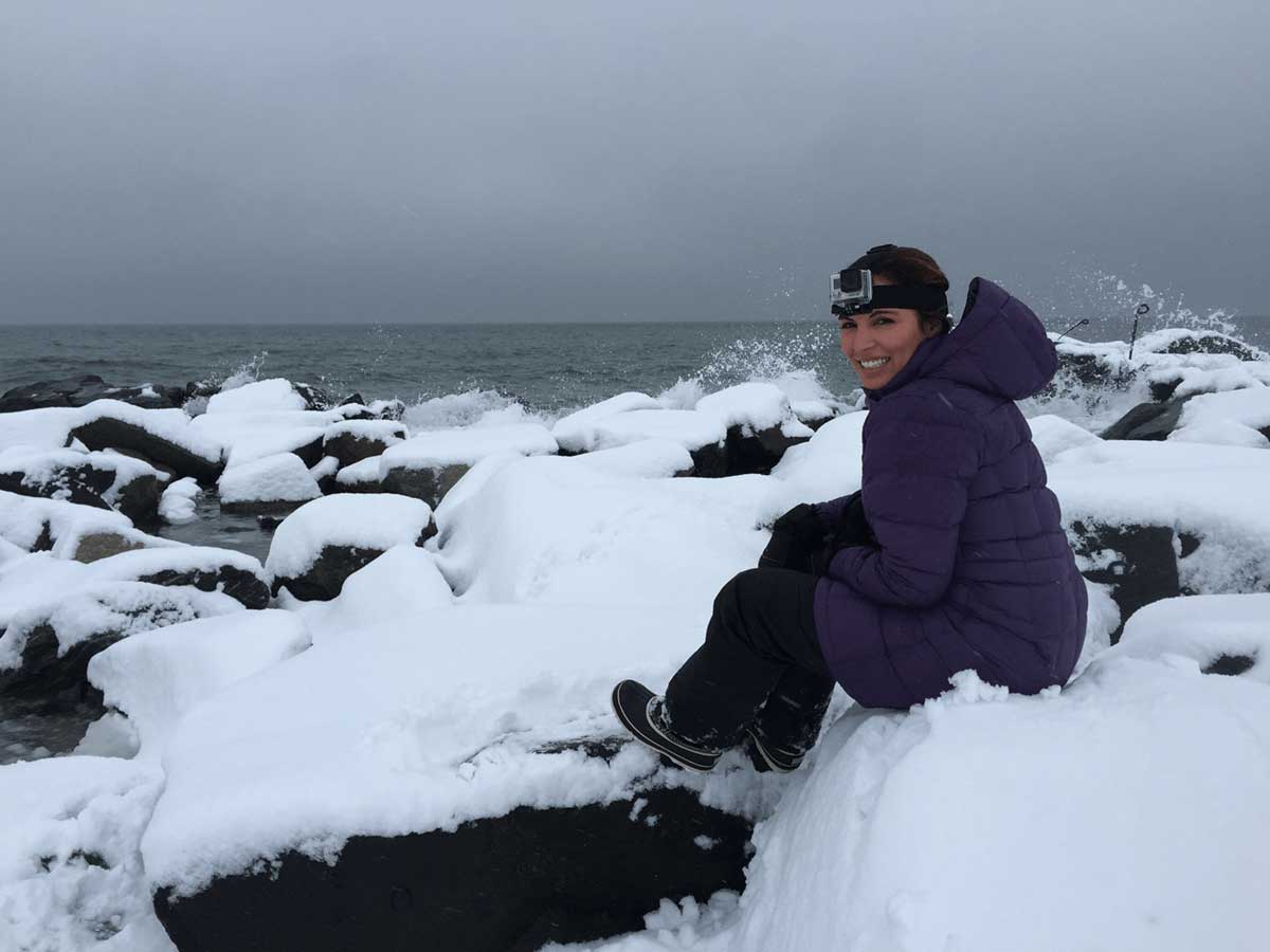student sitting on snow covered rocks in front of a large body of water