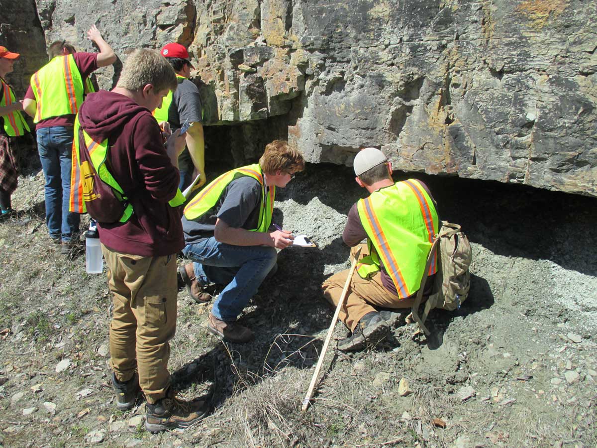 A group of people in yellow vests look under a large rock formation.