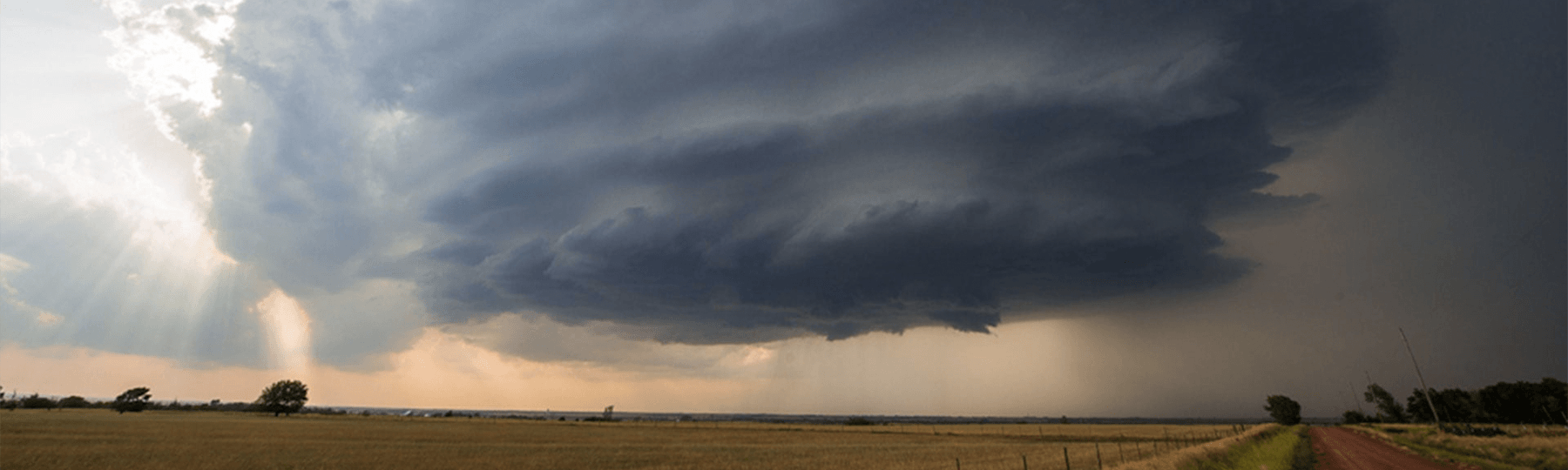 A dark storm cloud spins above a farm field.