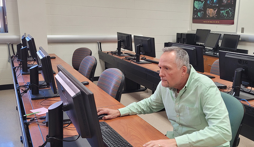 Geography faculty member in a green shirt sitting at a computer.