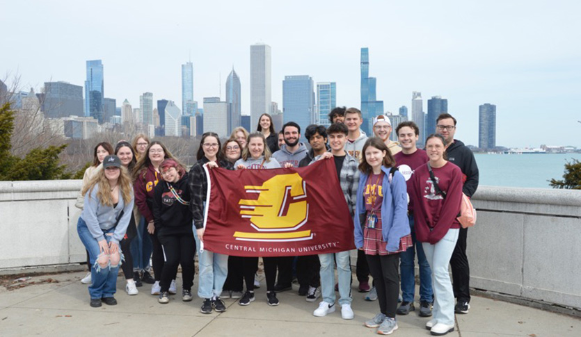 A group of Science and Engineering Residential College students holding at Central Michigan University flag with the city of Chicago in the background.