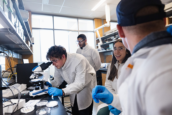 a group of people in lab coats looking through a microscope