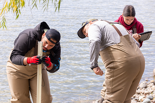 a group of people in overalls by water examining water samples inside a tall clear tube